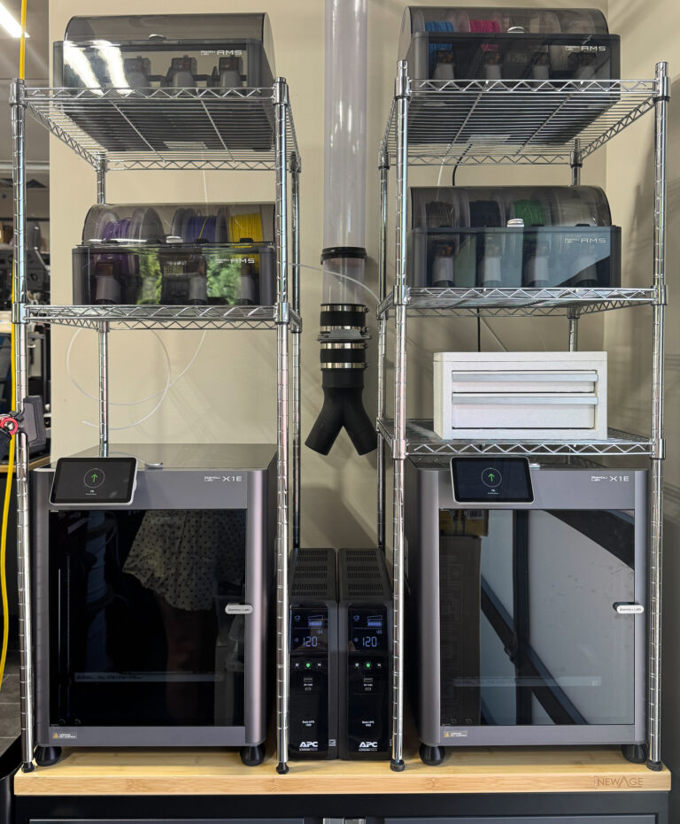 Two Bambu Lab X1E 3D printers side by side on a wire shelving unit, with filament and supplies stored above